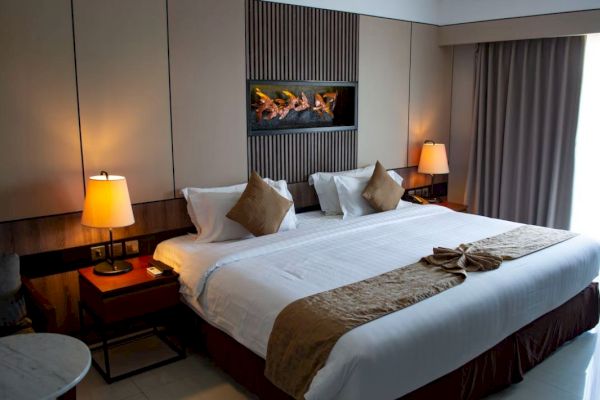 A cozy hotel room features a large bed with white linens, decorative pillows, and warm lighting from bedside lamps, creating a welcoming ambiance.