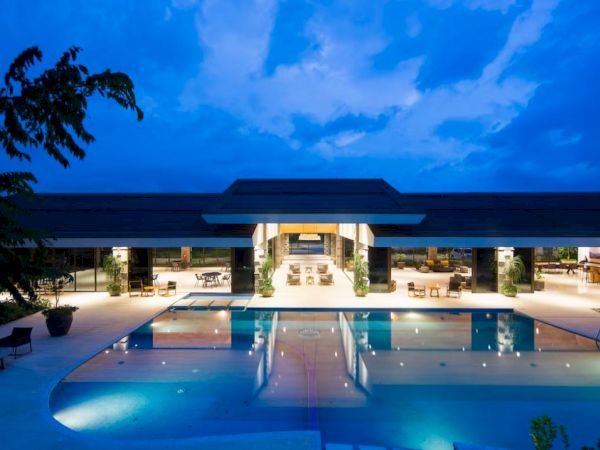 The image shows a modern building with an illuminated pool in the foreground under a twilight sky.