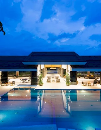 A luxurious poolside area with a modern building lit up at night under a blue sky, creating an inviting and serene atmosphere.