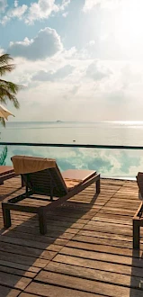 Lounge chairs and umbrellas overlook an infinity pool with a scenic ocean view under a partly cloudy sky, creating a relaxing atmosphere.