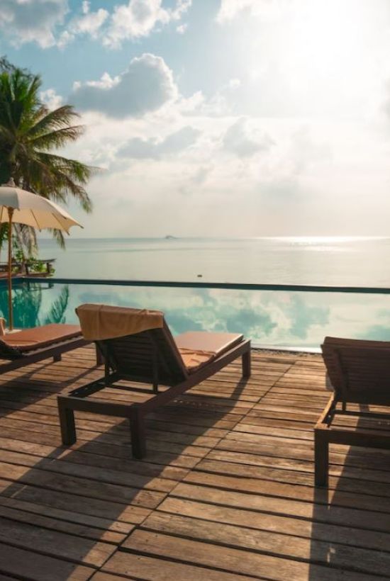 A serene poolside scene with lounge chairs, sun umbrellas, and a view of the ocean under a partly cloudy sky.
