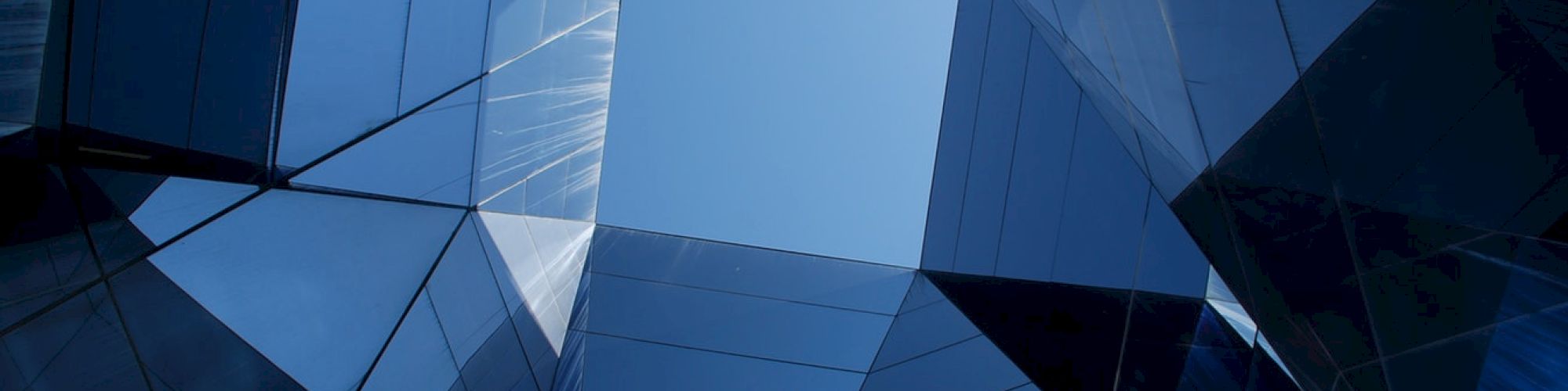 Geometric glass structures converge towards a central open sky, creating a modern and symmetrical architectural view.