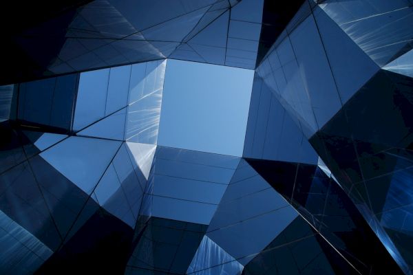 The image shows a geometric structure with mirrored panels reflecting the sky, creating an abstract, futuristic architectural view.