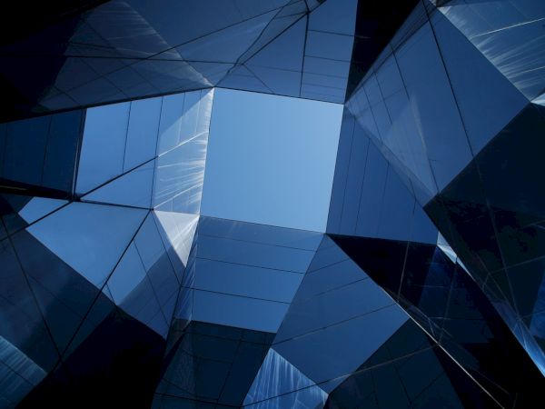 The image shows a geometric structure with mirrored panels reflecting the sky, creating an abstract, futuristic architectural view.