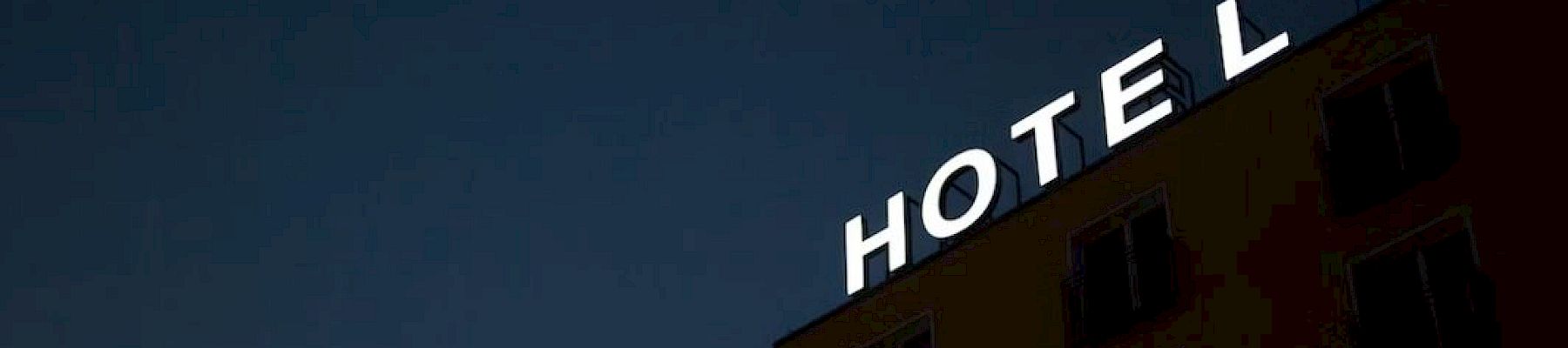 The image shows a building at night with an illuminated sign that reads "HOTEL," against a dark sky.