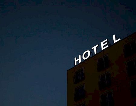 The image shows a building at night with an illuminated sign that reads "HOTEL," against a dark sky.
