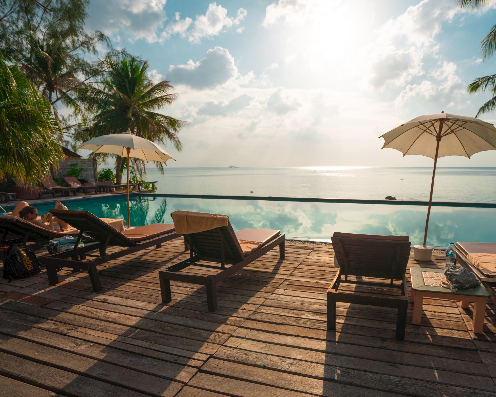 A serene beach scene with lounge chairs, umbrellas, and a calm ocean under a bright sky and palm trees.