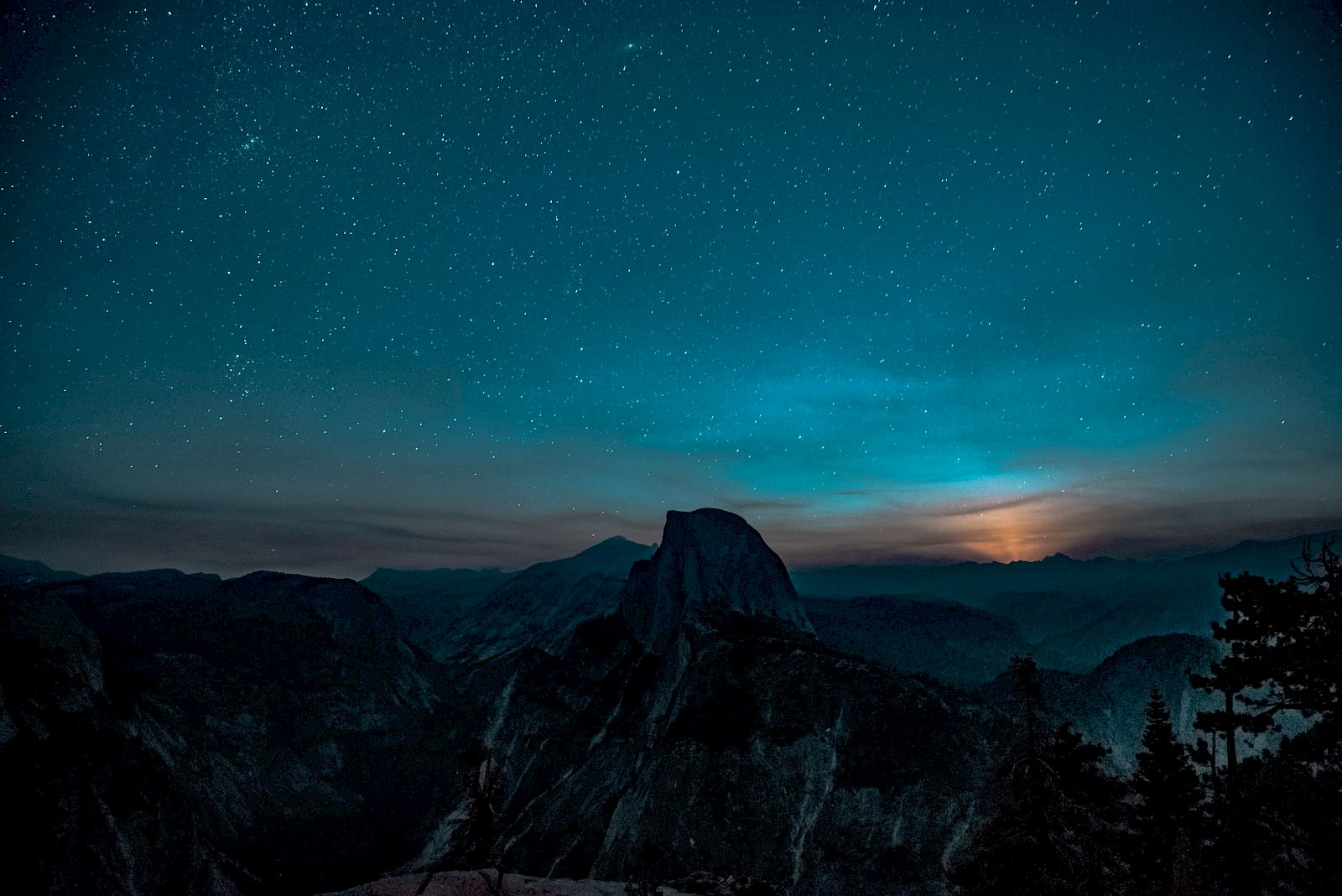 A starry night sky over a mountainous landscape with a prominent peak silhouetted against the horizon.