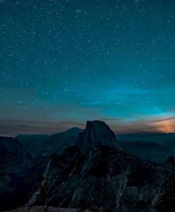 A silhouetted mountain landscape under a starry night sky with a glowing horizon.