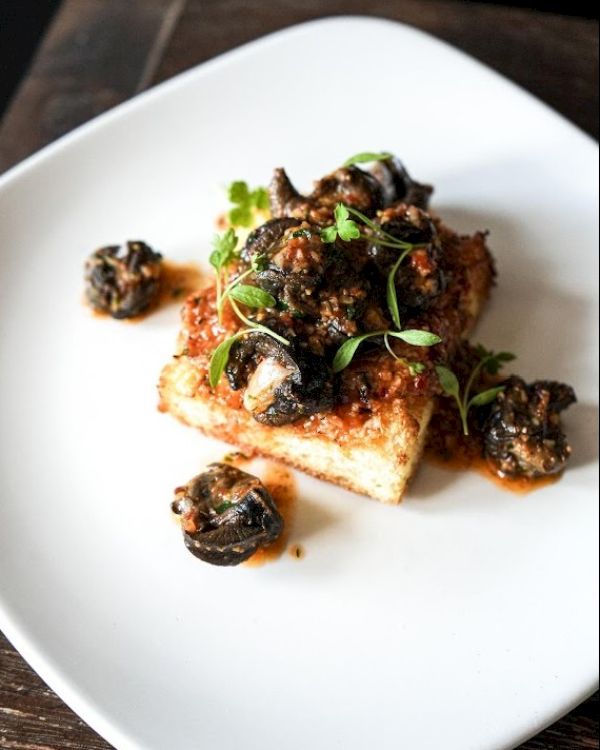 A dish featuring escargot atop crispy toast, garnished with fresh herbs on a white plate.