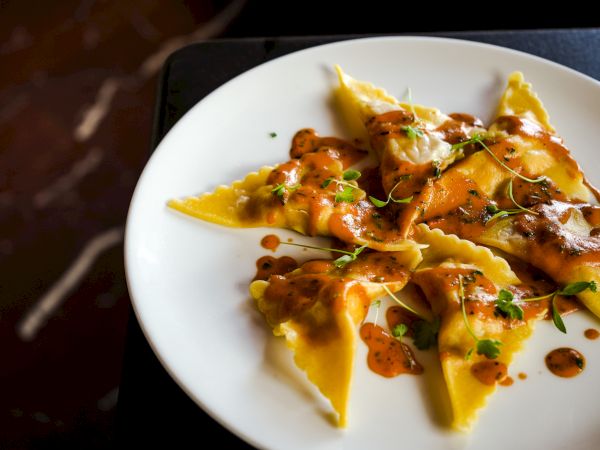 A plate of triangular ravioli topped with sauce and garnished with fresh herbs is artfully presented.