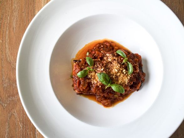 A plated beef stew with chunky sauce and fresh green basil leaves on top, served in a white bowl on a wooden table.