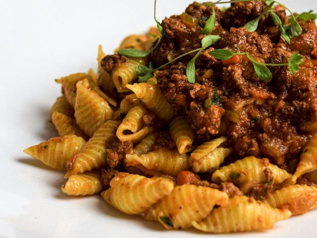 A plate of pasta with spirals topped by a chunky meat sauce and fresh herbs, served on a white dish.