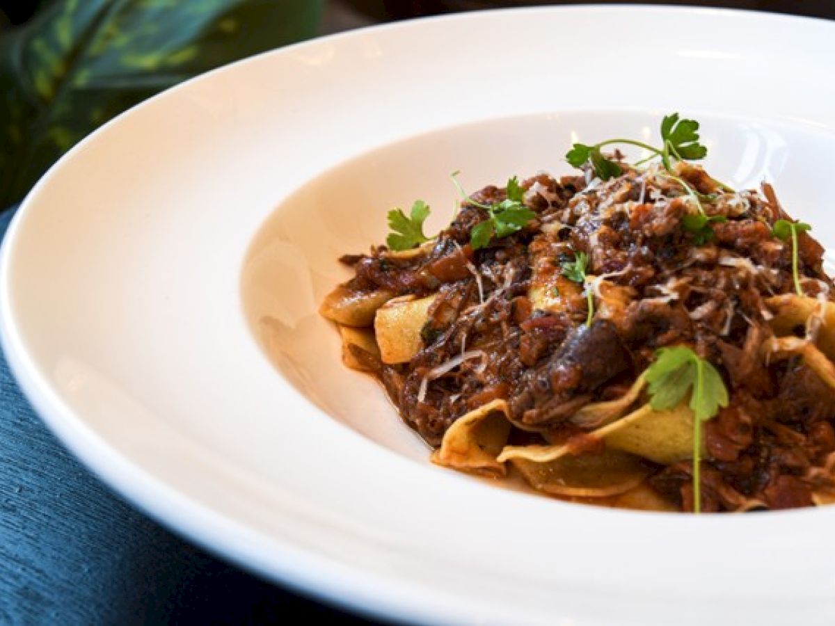 A plate of pasta topped with a rich meat sauce, garnished with parsley and grated cheese.