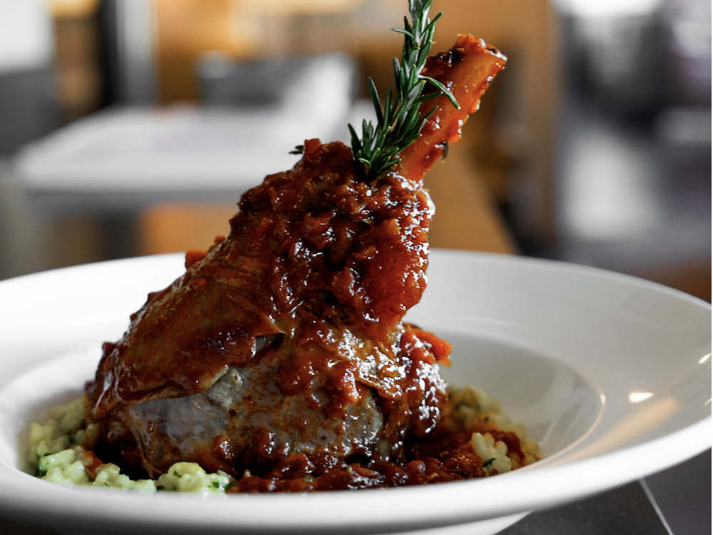 Delicately plated roasted meat and rosemary stem atop creamy mashed peas, rich glaze coating the tender meat. Delicious dish, perfectly plated.