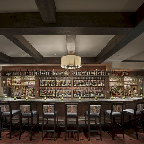 This image shows a well-lit, fully stocked bar with multiple shelves of bottles, bar stools, and warm, inviting décor and lighting.