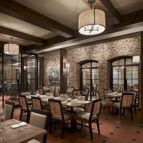 The image shows a cozy restaurant interior with brick walls, wooden beams, tables, and chairs neatly arranged, and decorative lighting fixtures.