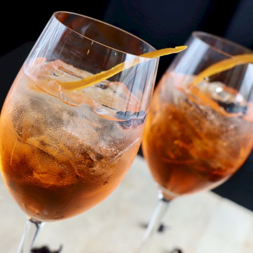 Two glasses of orange-hued cocktails with ice and a twist of citrus peel on top.