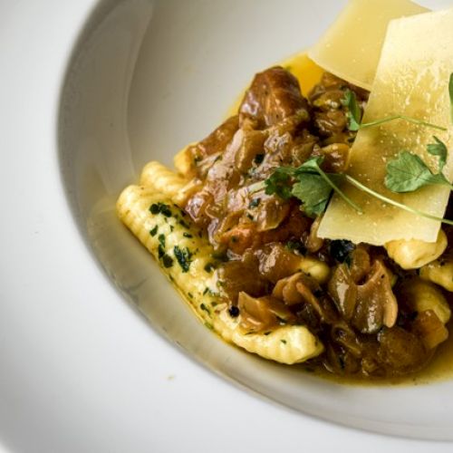 The image shows a plate of pasta topped with a savory sauce, garnished with cheese shavings and fresh herbs.