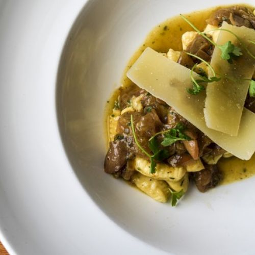 A plated dish with pasta, topped with mushrooms, herbs, and large slices of cheese, served on a white plate.