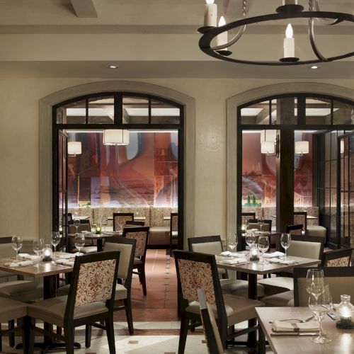 The image shows an elegant restaurant interior with neatly set tables, chairs, and soft lighting, creating a cozy and inviting atmosphere.