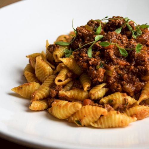 A plate of pasta topped with a rich meat sauce and garnished with fresh herbs, served on a white dish.