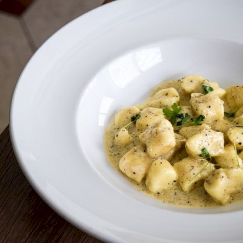 A white bowl of gnocchi in a creamy sauce, garnished with herbs.
