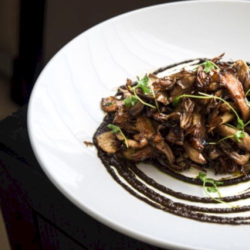 A plate of sautéed mushrooms garnished with fresh herbs, served on a decorative sauce swirl on a white dish.