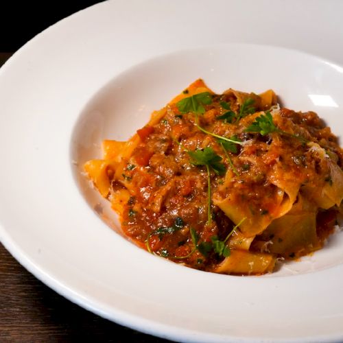 A plate of pasta with tomato-based sauce, garnished with herbs, served in a white bowl on a dark table.