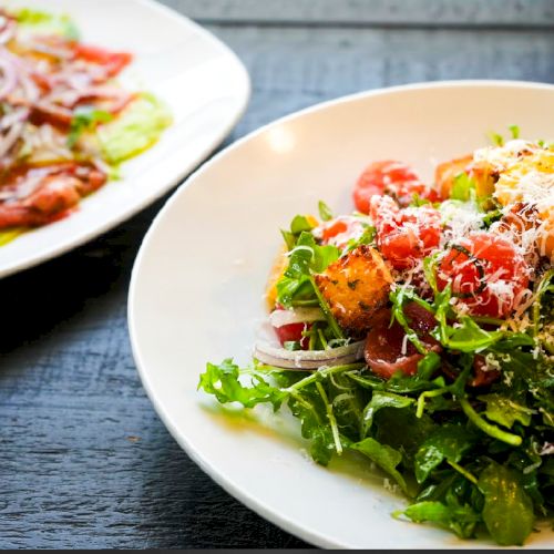 The image shows two plates of fresh salad with greens, tomatoes, onions, and cheese, placed on a dark table.