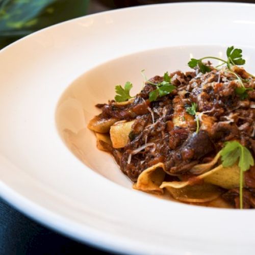 A dish of pasta topped with a rich meat sauce, garnished with fresh herbs and grated cheese, served on a white plate.