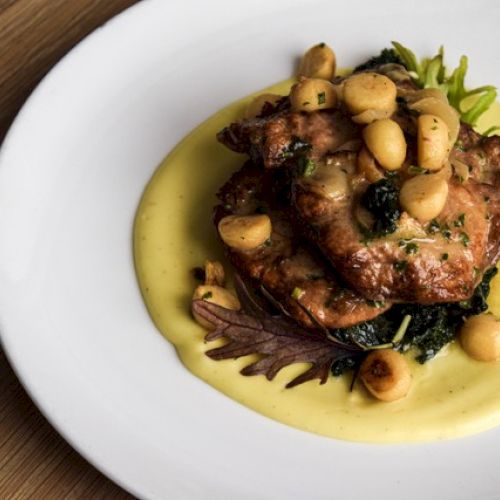 A gourmet dish with meat, vegetables, and sauce, garnished with small round pieces, served on a white plate.