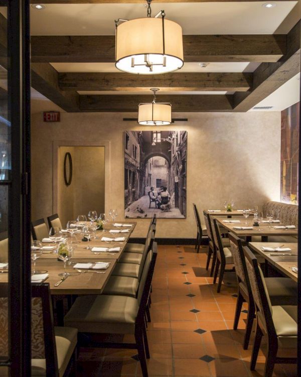 The image shows a cozy restaurant interior with wooden tables and chairs, warm lighting, and artwork on the walls.