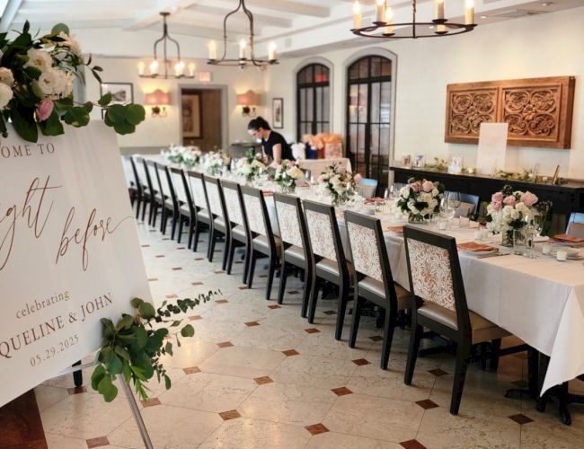 The image shows an elegantly set dining table in a decorated room, with a floral sign and stylish chairs, ready for an event.