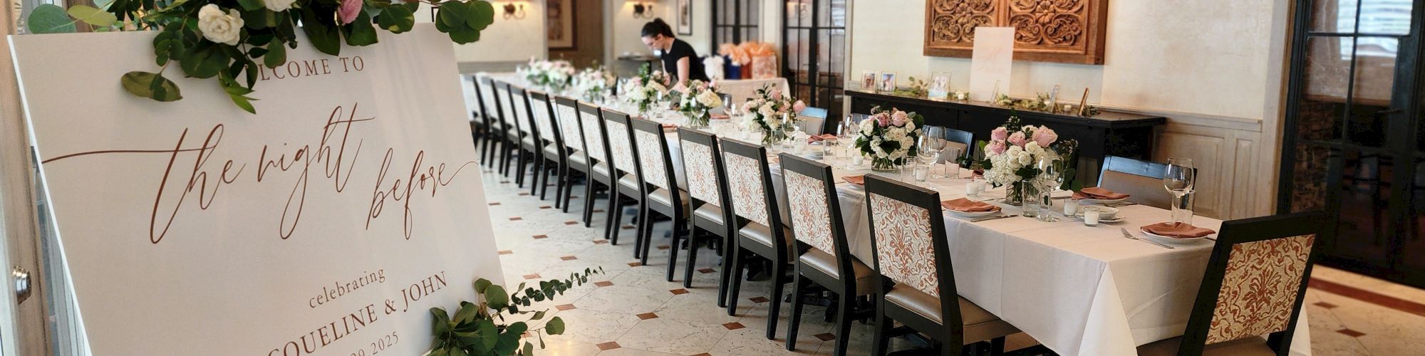 A long decorated banquet table with white linens, floral centerpieces, elegant place settings, and a &ldquo;the night before&rdquo; sign at the entrance; warm, classy event ambiance.