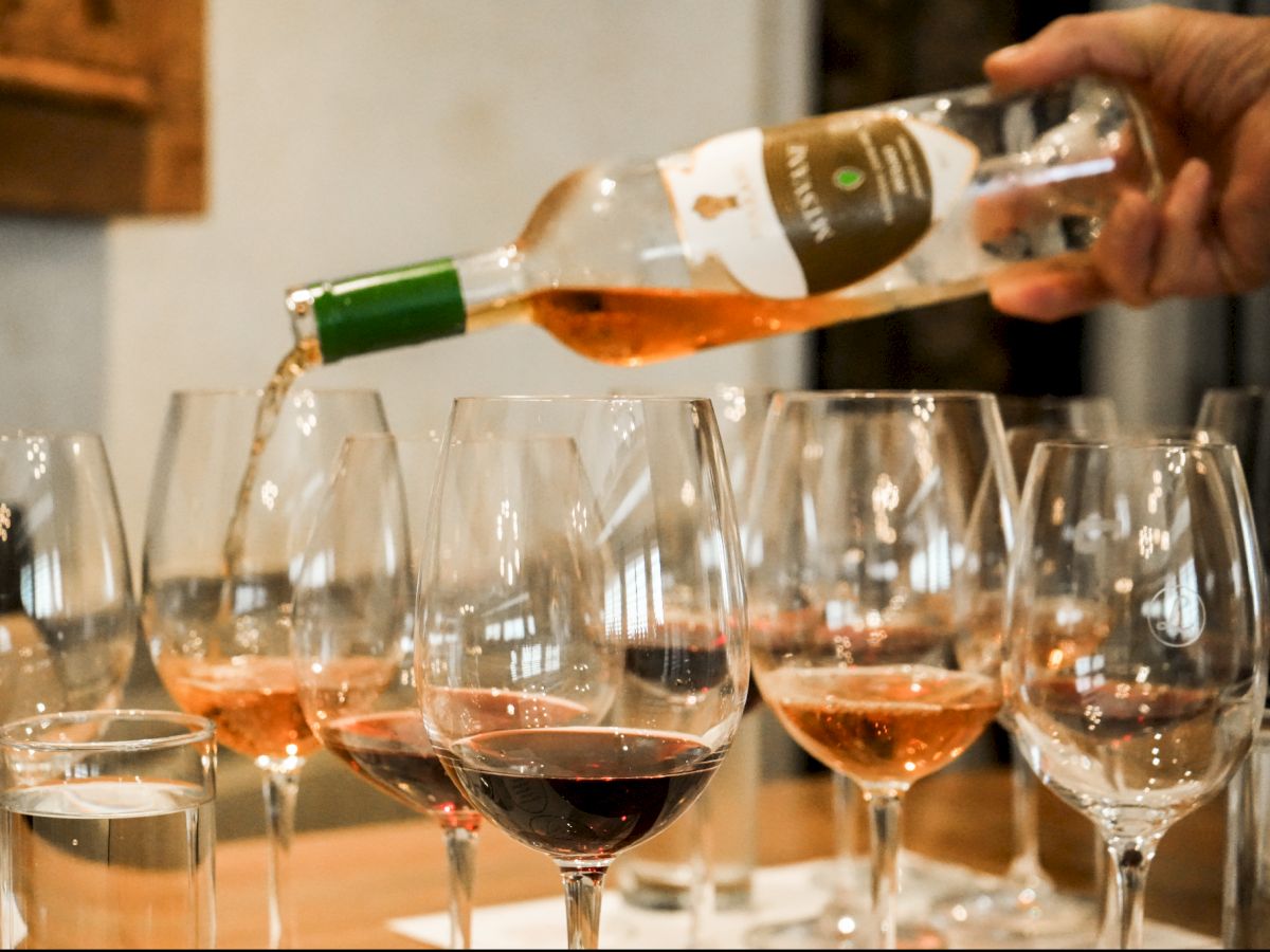 A person pours red wine from a bottle into several stemmed glasses at a table, with drinks splashing as it&rsquo;s served.