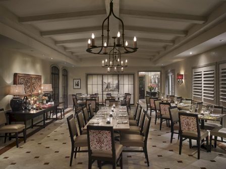 A formal dining room with multiple tables, elegant chairs, chandeliers, and warm ambient lighting.