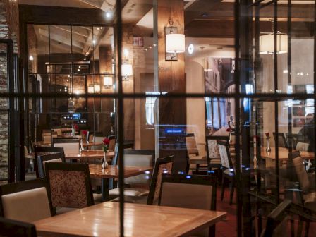 A warmly lit cafe with wooden tables, chairs, glass walls, and laptops on some desks, giving a cozy, modern coworking vibe.