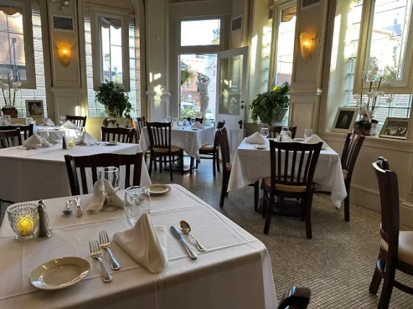 A bright, elegant restaurant dining room with neatly set tables, chairs, and warm wall lanterns.