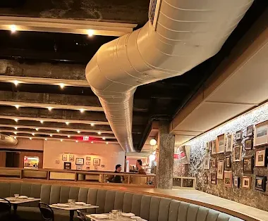 A cozy restaurant interior with a long bar, curved booth seating, tables set for dining, and framed photos on the walls.