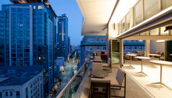 Rooftop terrace at twilight with modern seating, overlooking a cityscape of tall buildings and a lit street.