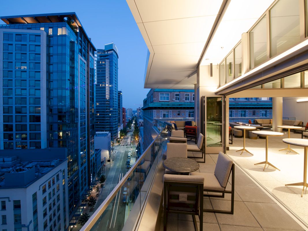 A modern rooftop terrace with seating offers a view of a cityscape with tall buildings at dusk, creating a stylish urban ambiance.