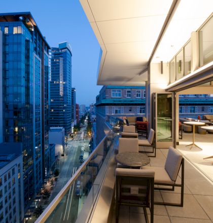 A modern rooftop terrace with seating, overlooking a city street filled with tall buildings at twilight, creating a sophisticated urban ambiance.