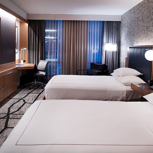 A hotel room with two double beds, a wall-mounted TV, a desk with a chair, and modern lighting creates a cozy atmosphere.