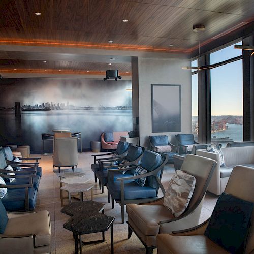 A modern lounge with stylish seating, large windows showcasing a scenic view, and a sophisticated interior.