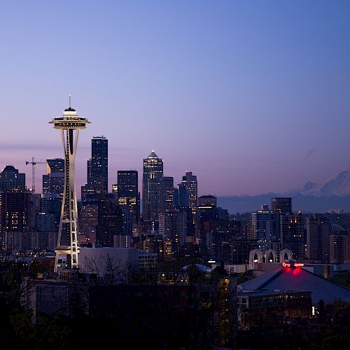 The image shows the Seattle skyline at dusk with the Space Needle and Mount Rainier in the background under a colorful sky.