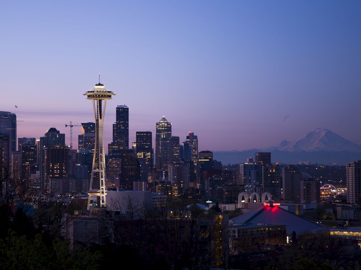 The image shows a city skyline at dusk, featuring a distinctive tower with a mountain in the background.