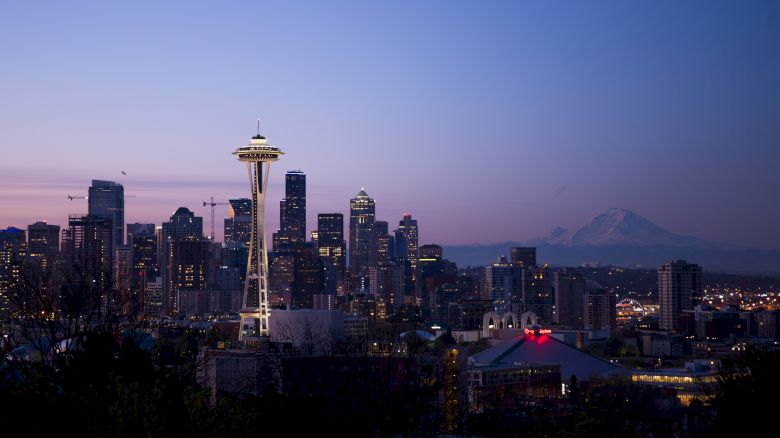 The image shows a city skyline at dusk, featuring a distinctive tower with a mountain in the background.