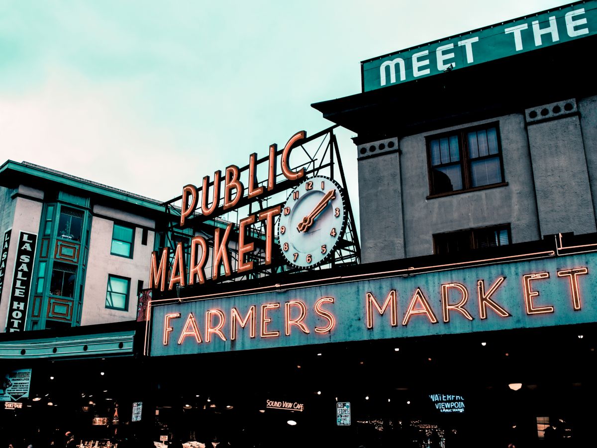 The image shows a neon sign for "Public Market" and "Farmers Market" with a clock, against a building backdrop.