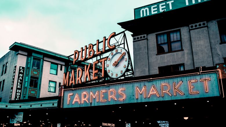 The image shows a neon sign for "Public Market" and "Farmers Market" with a clock, against a building backdrop.